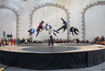 sur une structure avec des trampolines, six danseurs sont en vol