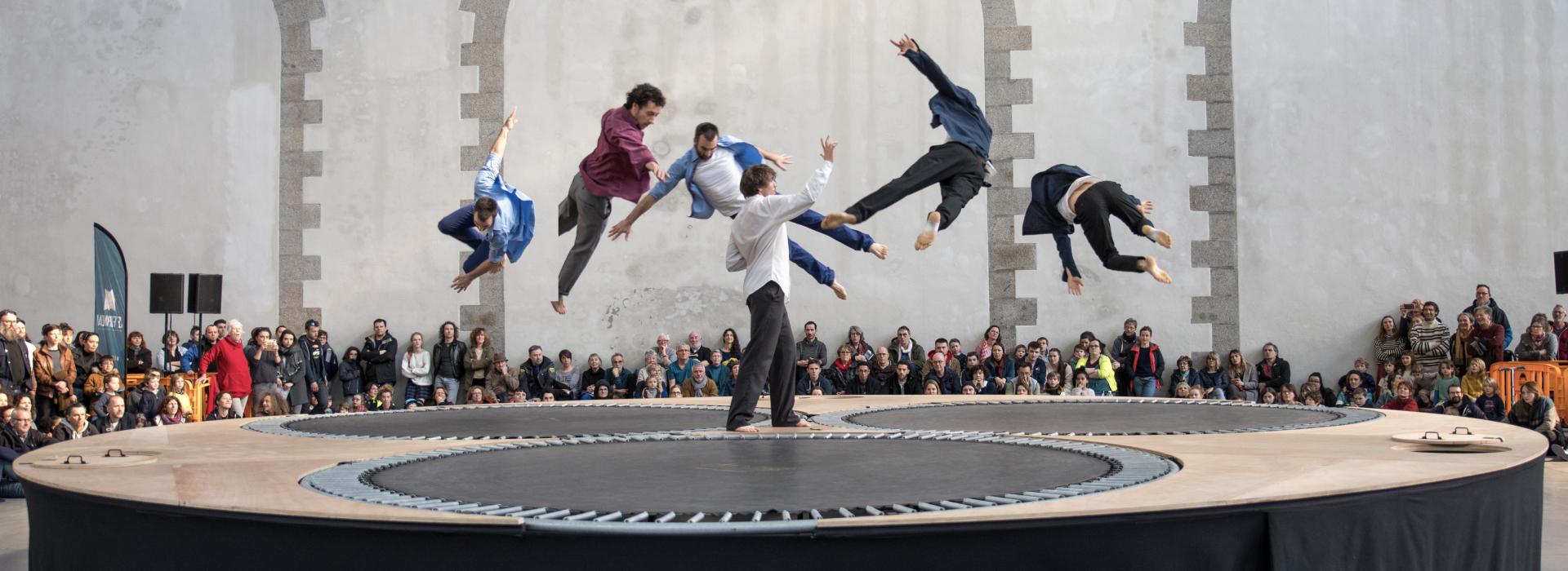 sur une structure avec des trampolines, six danseurs sont en vol